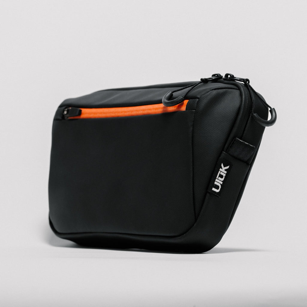 Three-quarter front view of the black TPU sling bag showing the orange zipper.