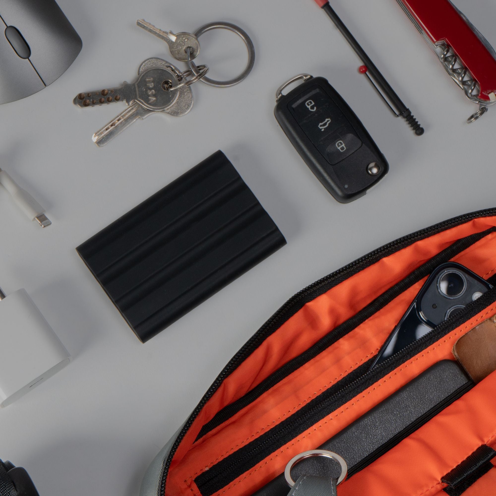 Everyday carry gear arranged next to the open orange interior pocket of the black sling bag.