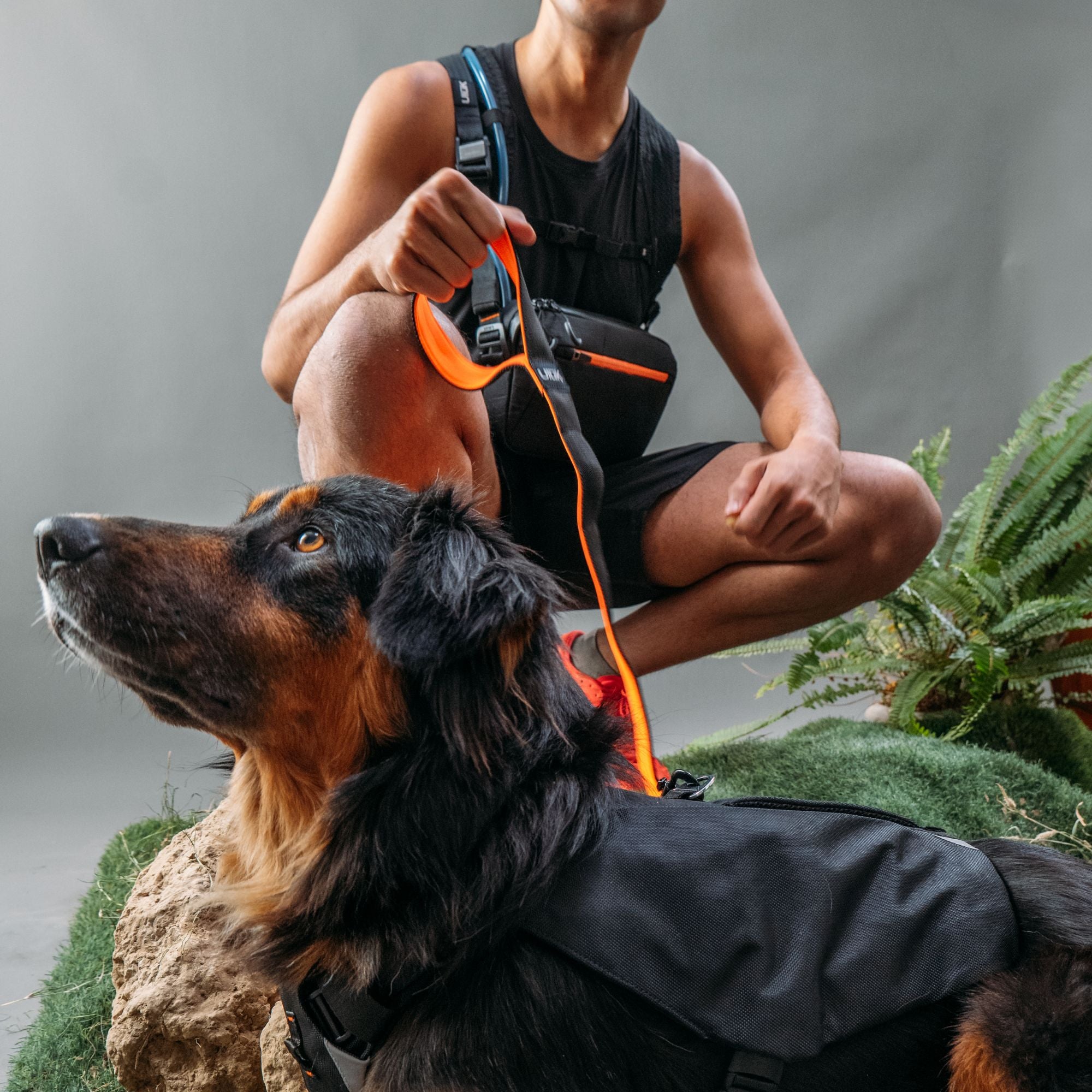 A person crouching with a dog while wearing the black Ulūk Outdoors TPU sling bag.