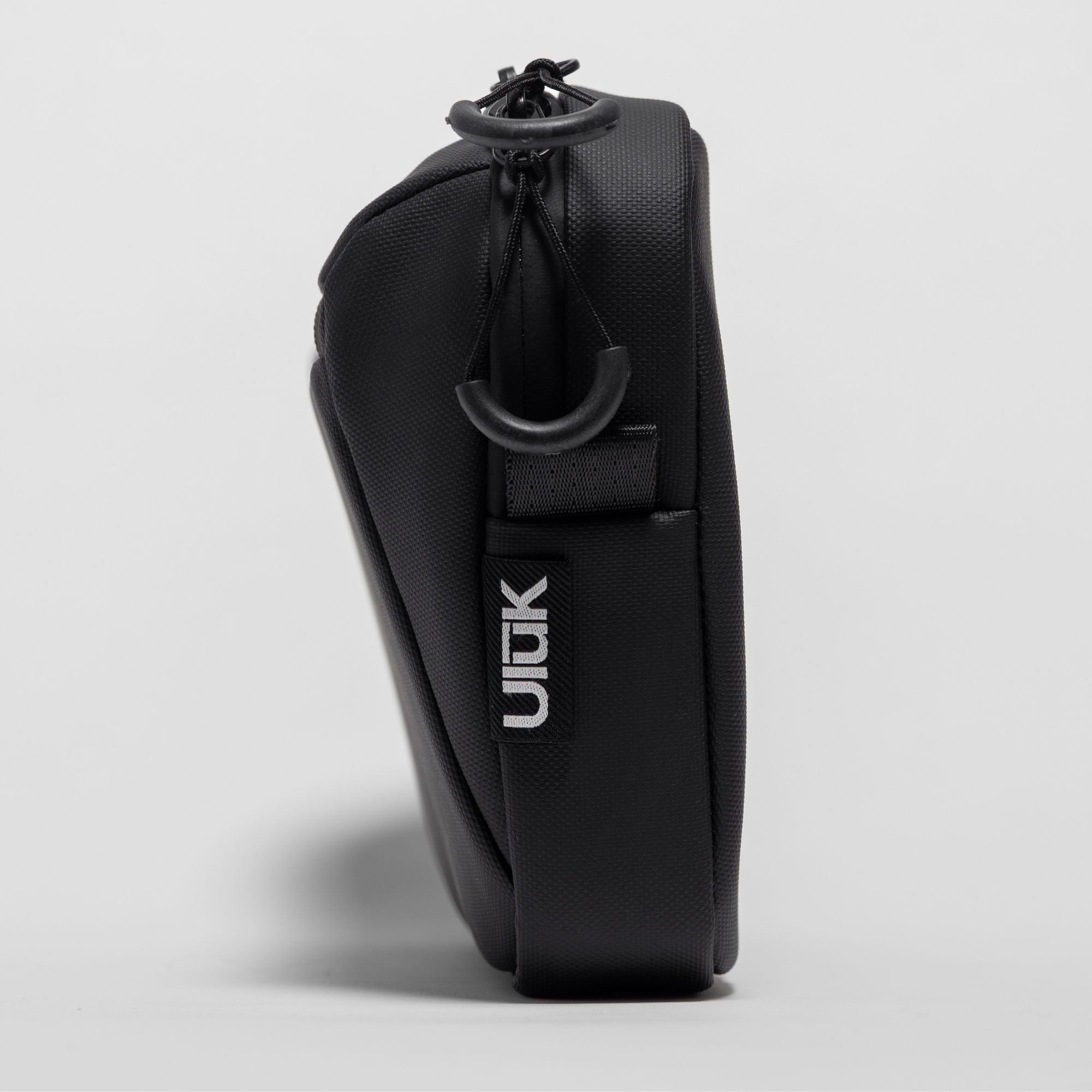 Side profile view showing the slim depth and zipper loops of the black sling bag.